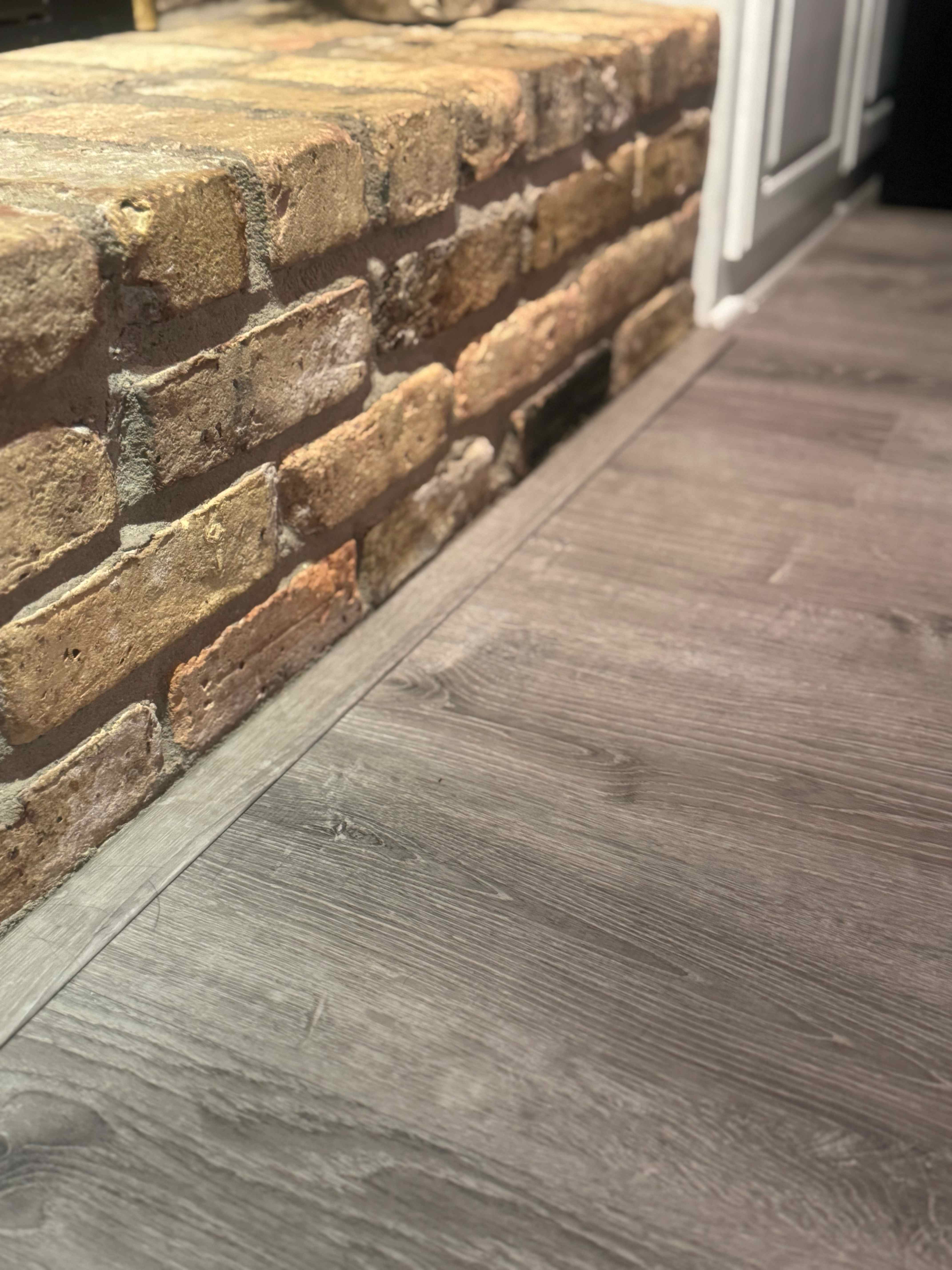 Precision trim work where hardwood flooring meets brick wall with perfect finishing
